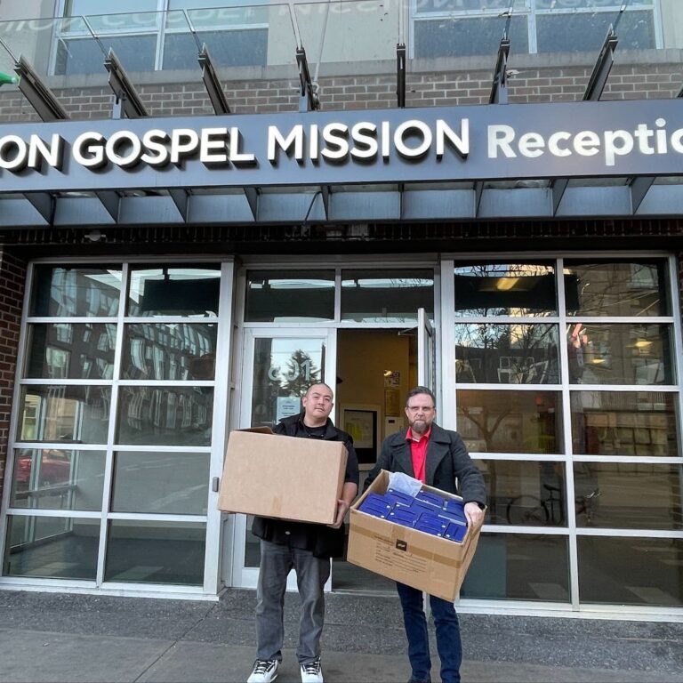 Representatives from Evolution Fulfillment and Sealskinz® hold boxes of donations in front of the Union Gospel Mission in Vancouver's Downtown Eastside.