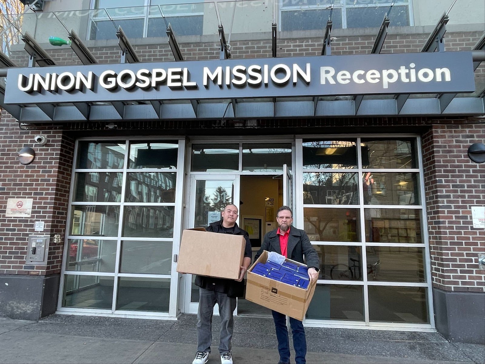 Representatives from Evolution Fulfillment and Sealskinz® hold boxes of donations in front of the Union Gospel Mission in Vancouver's Downtown Eastside.