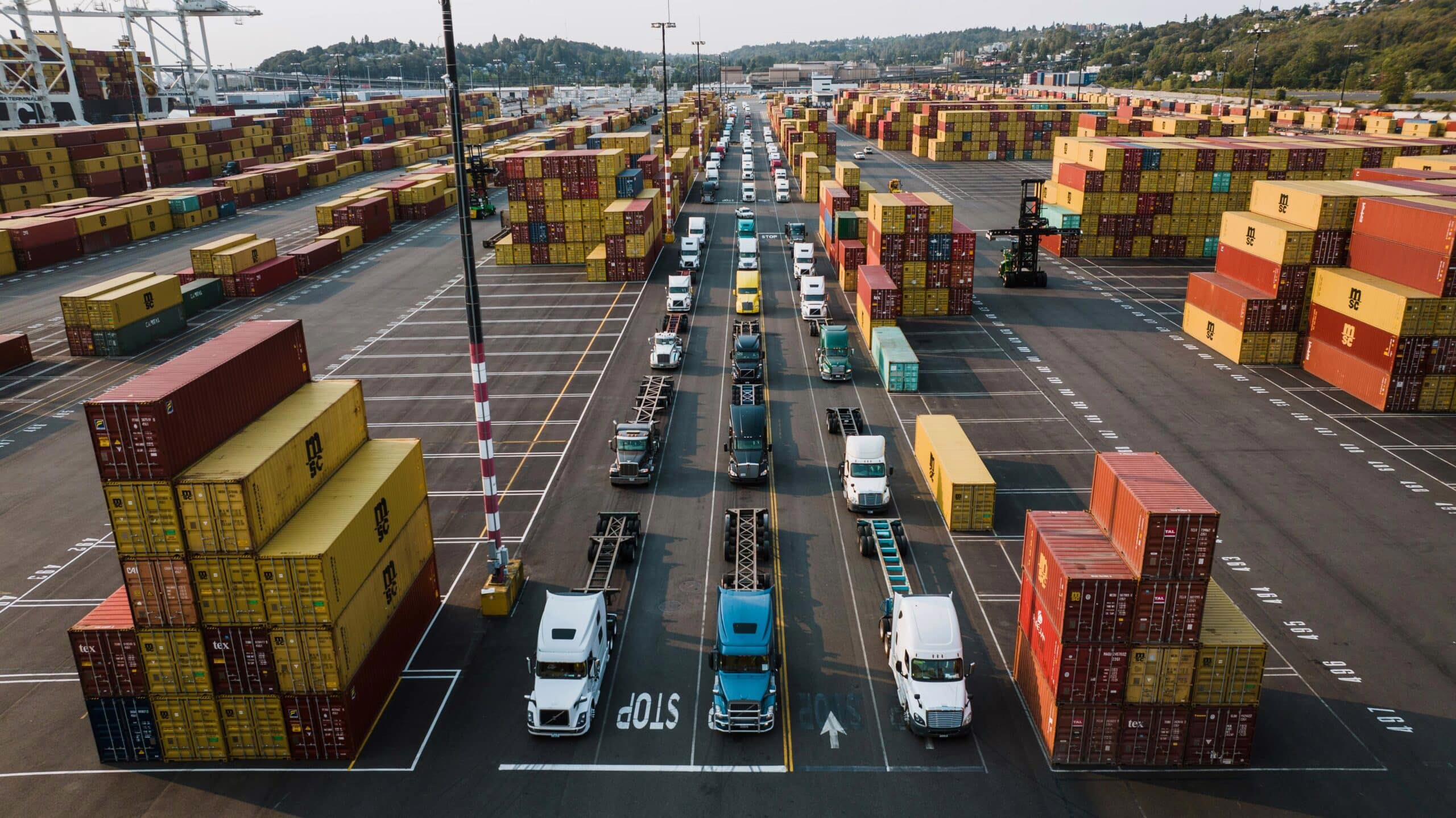 Shipping containers and trucks line up in a busy port.