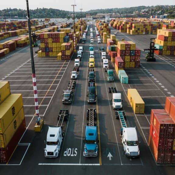 Shipping containers and trucks line up in a busy port.