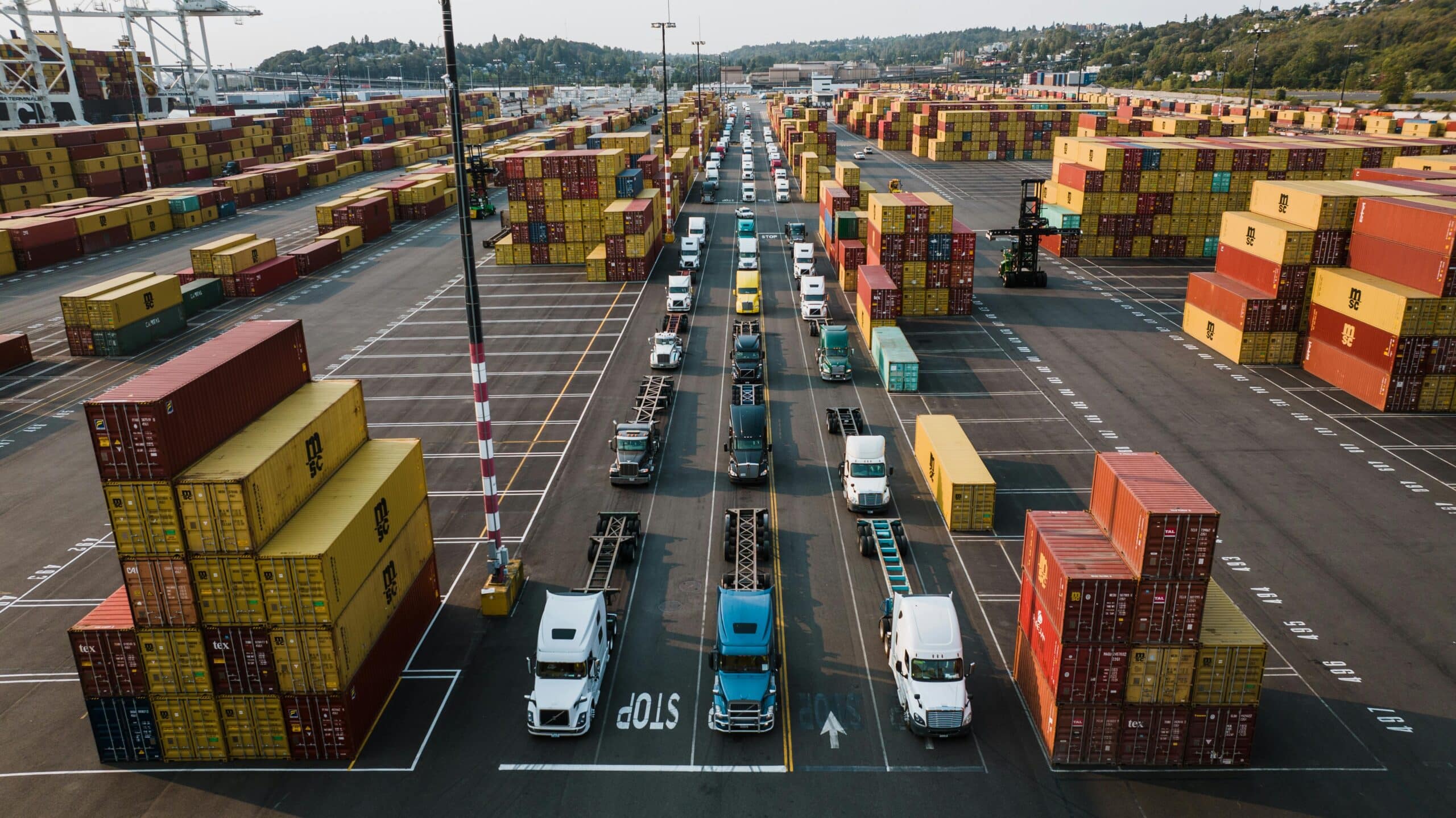 Shipping containers and trucks line up in a busy port.
