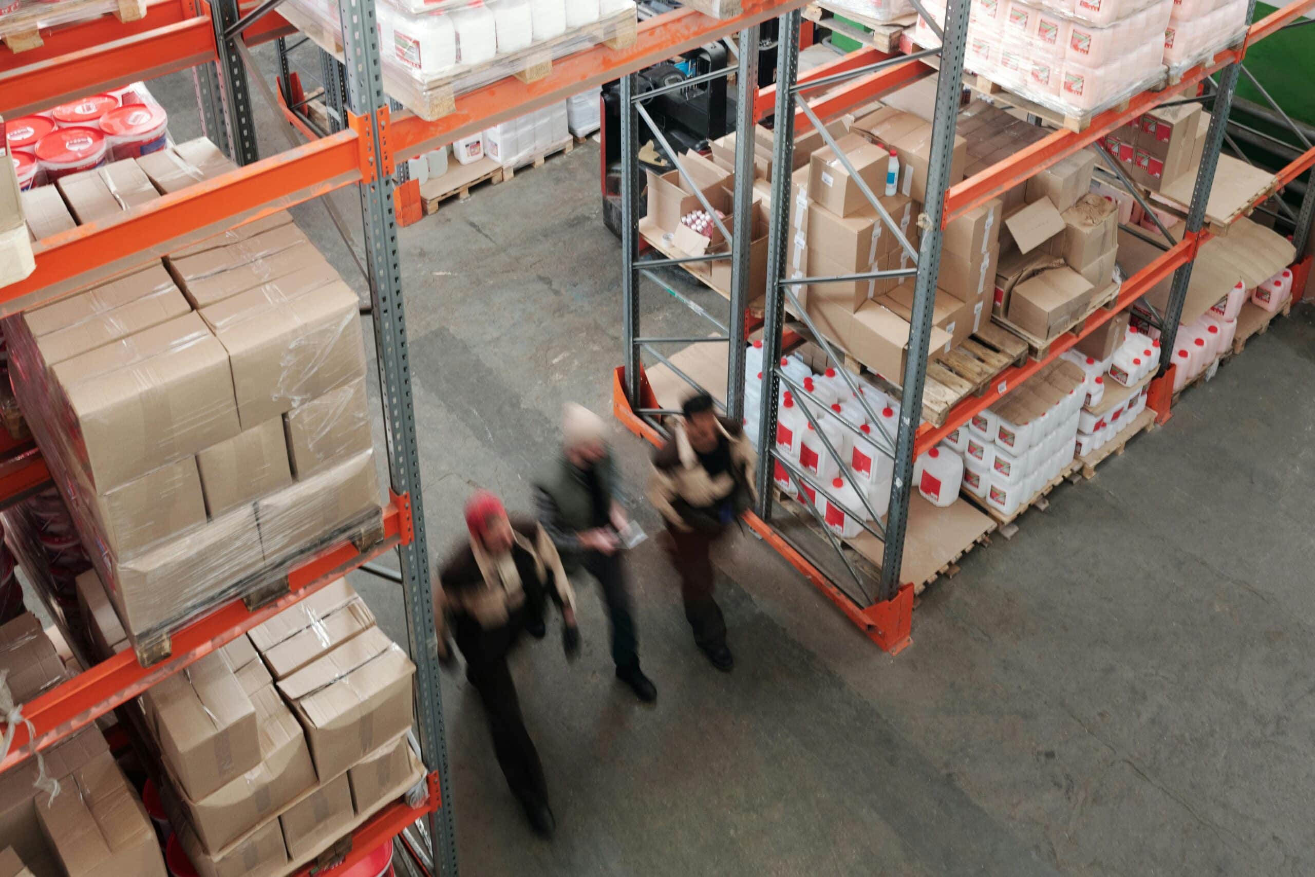 Workers walk through rows of tall shelves in a fulfillment warehouse storing goods.