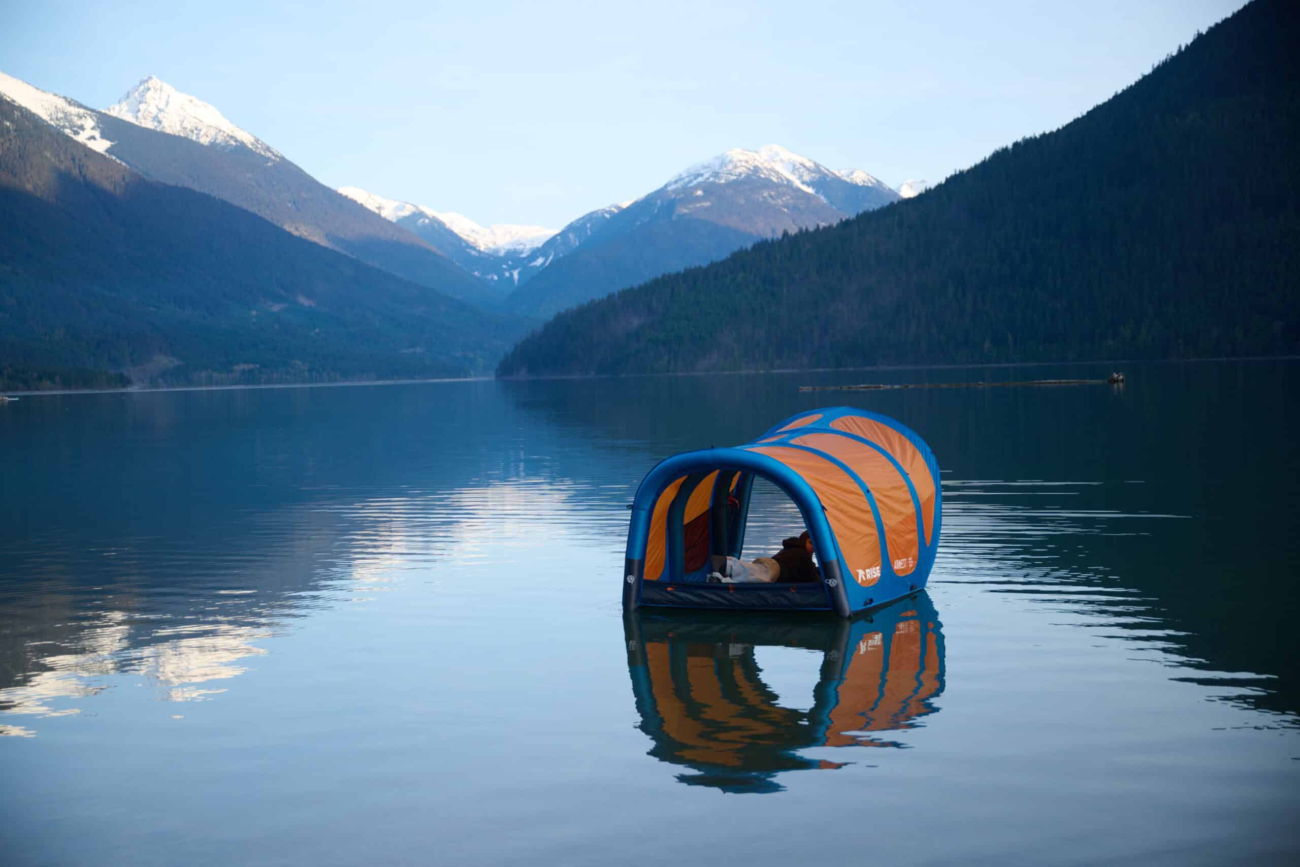 An inflatable test floats on a lake with mountains in the background.