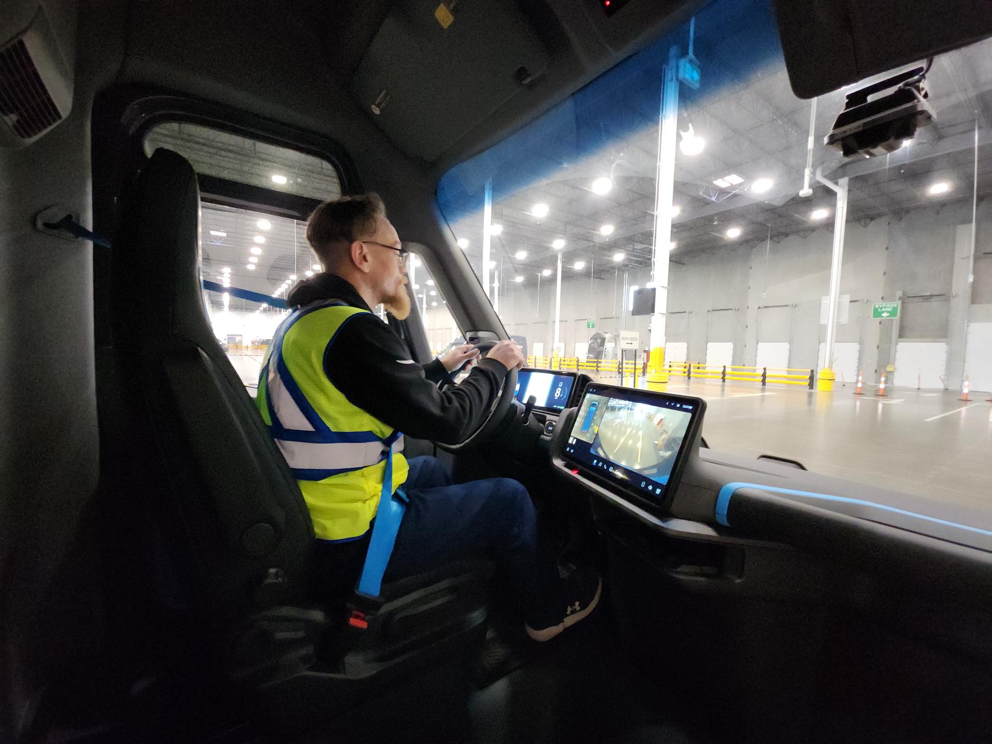 A man drives a new Amazon Rivian Electric Delivery Van (EDV) out of a warehouse