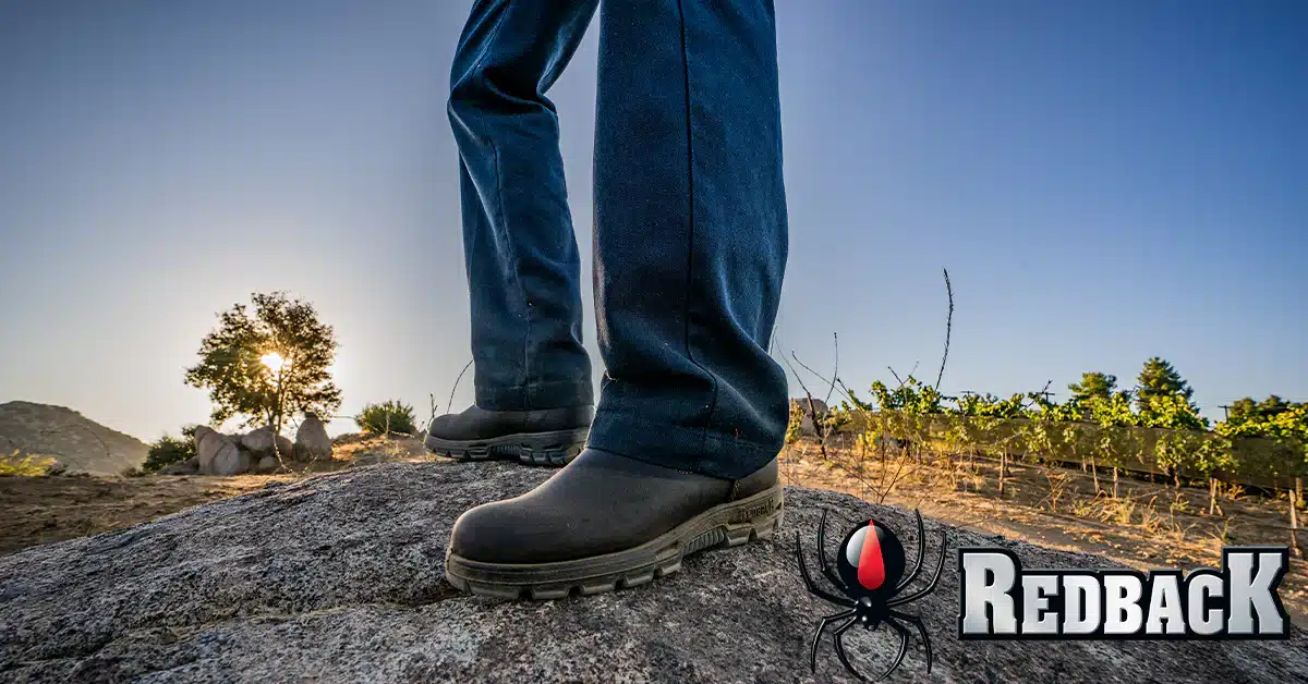 A person's legs wearing Redback Boots and standing on a rock.