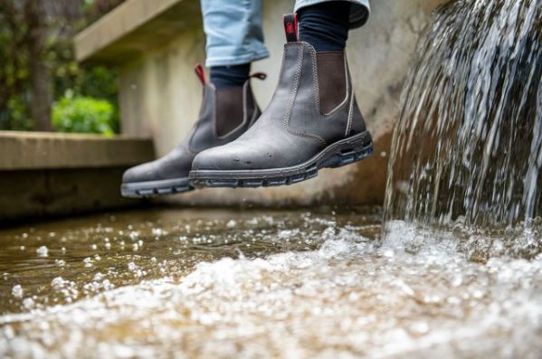 Two feet wearing Redback Boots hover over water.