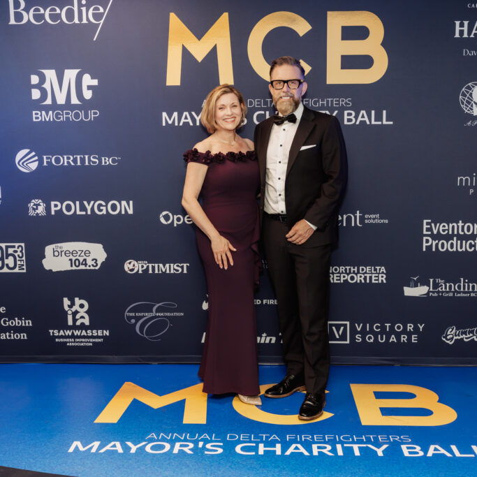Evolution Group Of Companies Founders, Gwen and Ben Martin attend the Annual Delta Firefighters Mayor’s Charity Ball. The stand in front of a sign that says MCB Mayor's Charity Ball.