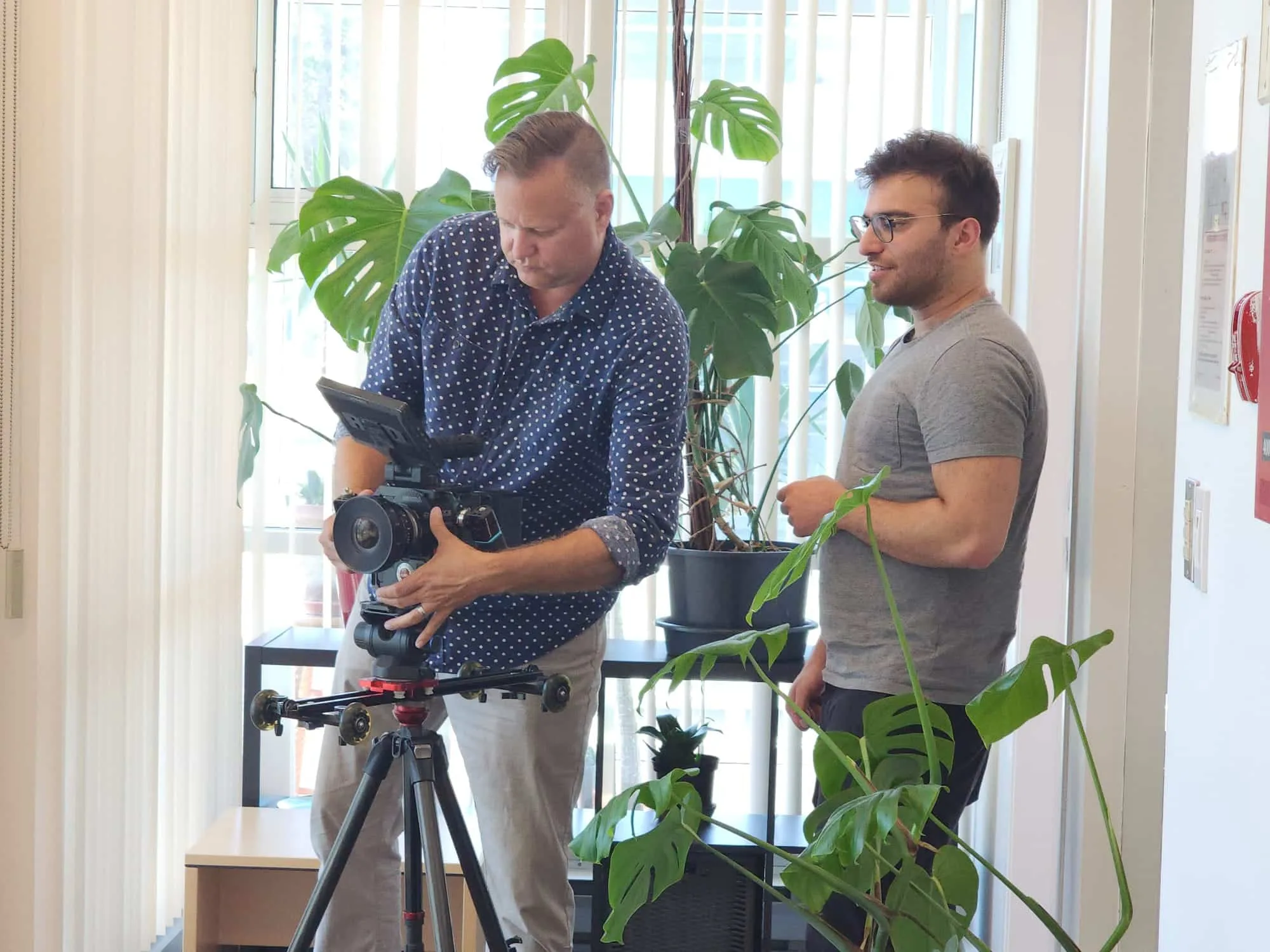 Two male filmmakers set up a video camera in an office environment.